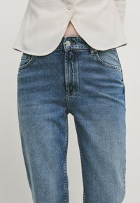 Denim jeans in a medium blue wash, featuring a standard five-pocket design, belt loops, and a zipper fly with button closure.