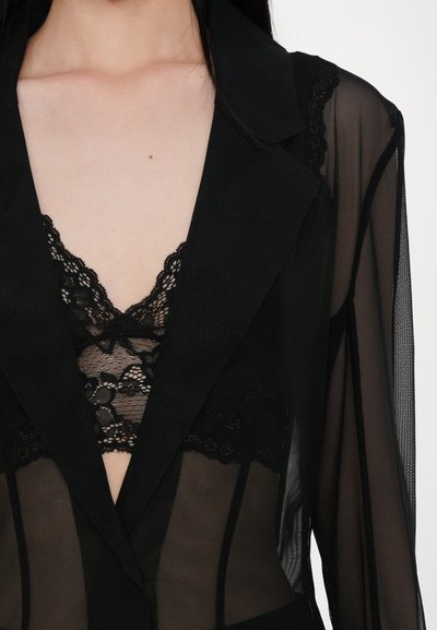 Schwarzer transparenter Blazer mit Reverskragen und langen Ärmeln, über einem schwarzen Spitzentop getragen. Verfügt über zarte Spitzelemente und einen tiefen V-Ausschnitt.
