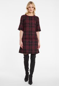 Robe en tweed à carreaux rouges et noirs avec des manches courtes et des accents à franges. Associée à des bottes en cuir noires montantes.