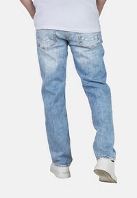 Jeans in denim azzurro chiaro con una vestibilità rilassata, dotati di due tasche posteriori e un effetto lavato, abbinati a sneakers bianche.