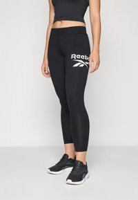 Sorte leggings med høy midje, med en hvit Reebok-logo. De er laget av et glatt, elastisk stoff og har en tettsittende design.