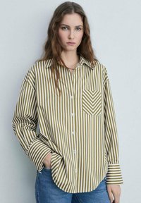 Camicia a bottoni in cotone con strisce verticali bianche e verde oliva. Presenta una tasca con un motivo a zigzag sul lato sinistro.
