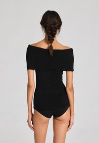 Juodas off-the-shoulder marškinėlis, pagamintas iš minkštos medžiagos, prigludusio silueto, ilgomis rankovėmis ir lygiu paviršiumi. Derinamas su atitinkančiomis juodomis šortais.