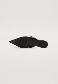 Chaussure noire à talon haut avec un bout pointu et un dessus lisse. Elle possède une fine sangle à la cheville et une semelle texturée pour plus d'adhérence.
