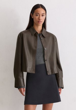 Bruine leren cropped jack met een kraag, knoopsluiting en lange mouwen over een grijze geribbelde sweater en een zwarte rok.