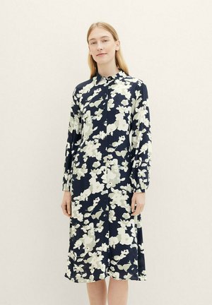 Robe à boutons florale en bleu marine avec des motifs blancs et vert clair, à manches longues et à coupe décontractée qui tombe juste en dessous des genoux.