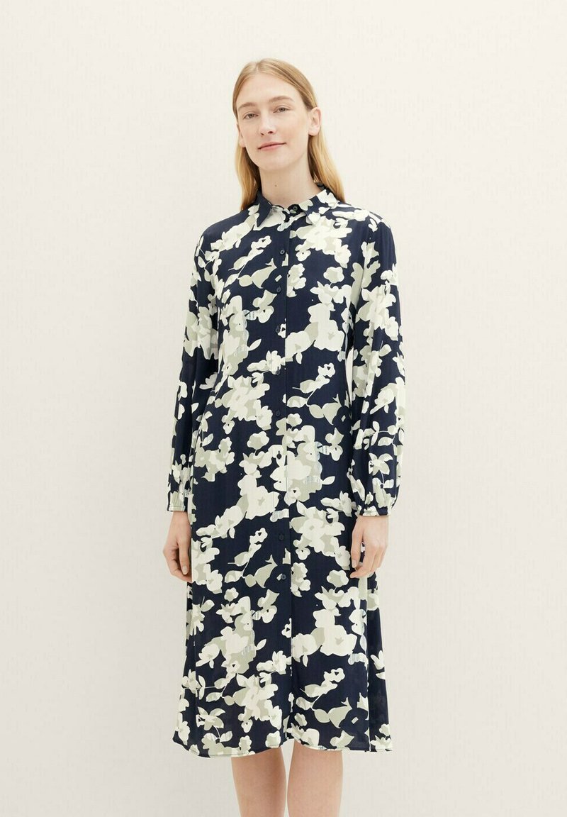 Robe à boutons florale en bleu marine avec des motifs blancs et vert clair, à manches longues et à coupe décontractée qui tombe juste en dessous des genoux.