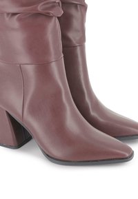 Par de botas de tobillo de cuero marrón con punta afilada, con un eje arrugado y tacones de bloque sobre fondo blanco.