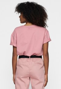 T-shirt di cotone rosa con maniche arrotolate, vestibilità rilassata e un'etichetta discreta sul retro. Abbinato a pantaloni rosa con vita elasticizzata e cintura nera.