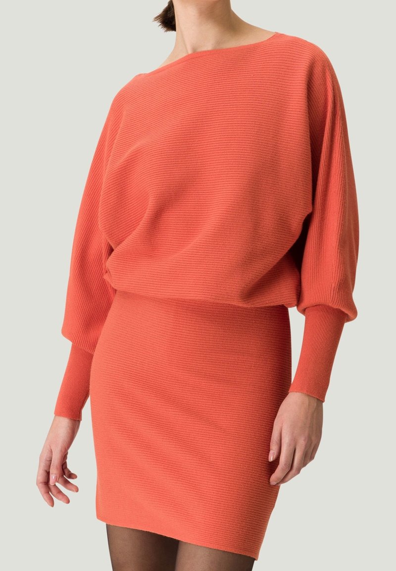 Robe tricotée côtelée corail avec un large col bateau, des manches longues et une silhouette ajustée, présentant un tissu texturé et un design sans couture.