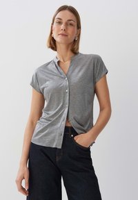 Camicia grigia a maniche corte con colletto alla cinese, caratterizzata da una vestibilità comoda e una texture liscia. Abbinata a jeans scuri.
