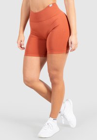 Hoge taille, roestkleurige fietsshorts van rekbaar materiaal, met een gladde textuur en een aansluitend ontwerp. Gecombineerd met witte sneakers.