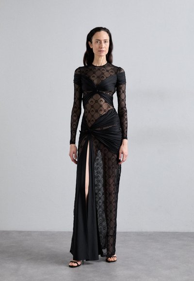 Czarna sukienka z przezroczystego materiału o wzorze, z węzłowymi detalami, długimi rękawami i rozcięciem sięgającym uda z jednej strony. Gładka, elegancka faktura.