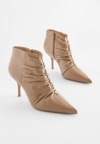 Bottines en cuir tan avec un bout pointu, un design froncé et une fermeture éclair sur le côté. Talon stiletto pour plus de hauteur et d'élégance.