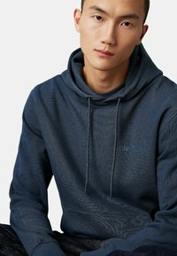 Felpa blu navy con un motivo testurizzato, cappuccio con cordino e tasca a marsupio. Presenta un logo sottile dello stesso colore sul petto.