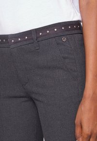 Donkergrijze pantalons met een soepele textuur, voorzien van een gespikkelde zwarte tailleband en accenthardware. Zijzakken zijn zichtbaar.