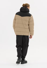 Puffjacka i brunt med svart huva och axlar, med quiltat mönster. Parat med lösa svarta cargobyxor och svarta sneakers.