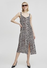 Leopardo rašto suknelė su plonais petnešėles, v-žuvo kaklo iškirpte, iki kelių, priekyje įpjova, plazdančio audinio, dėvima su juodais aukštakulniais bateliais ir akinių nuo saulės.