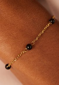 Armband aus Gold mit schwarzen Perlenakzenten. Die Kettenglieder sind zart, und die Perlen sind sphärisch mit einer glänzenden Oberfläche.