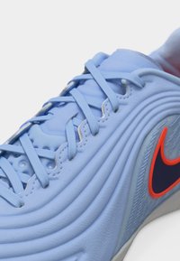 Jasnoniebieski but sportowy z zaokrąglonymi prążkami, pasującymi sznurowadłami oraz ciemnoniebieskim logo Nike w kształcie haka z czerwonym obramowaniem po bokach.