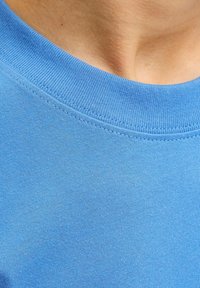 Κοντινό πλάνο του λαιμού και του άνω μέρους του στήθους ενός ατόμου που φοράει έν α γαλάζιο ριμπ πουλόβερ με λαιμόκοψη crewneck.