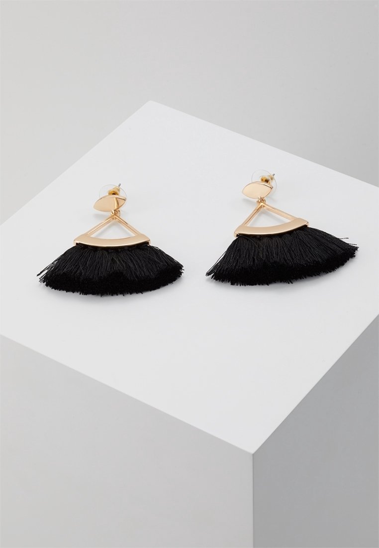 Paire de boucles d'oreilles triangulaires dorées avec des pampilles noires en forme d'éventail, présentées sur un cube blanc avec un fond gris.