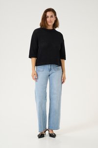 Black knitted cropped sweater with short sleeves, paired with light blue wide-leg jeans and black heeled mules. Plain background.