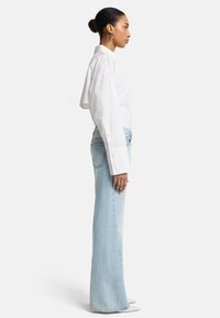 Chemise blanche à manches longues avec épaules basses, associée à un jean évasé bleu clair. Tissu lisse avec des poignets à boutons et des poches latérales.
