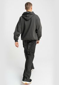 Ciemnoszara, oversize bluza z dużym kapturem, zestawiona z luźnymi czarnymi spodniami cargo. Model noszący czarne trampki z białymi akcentami.