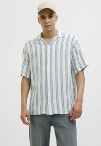 Chemise boutonnée en tissu léger avec des rayures verticales bleues et blanches, à manches courtes, et un col cranté. Associée à un jean en denim clair.