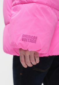 Svetlo ružová prešívaná bunda s lesklým povrchom. Má elastické manžety a viditeľné biele logo "AMERICAN VINTAGE".