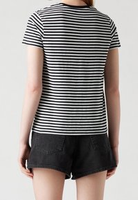 Czarny i biały w paski bawełnowy T-shirt z krótkimi rękawami, okrągłym dekoltem i lekko zaokrąglonym hemem, noszony z czarnymi szortami dżinsowymi.