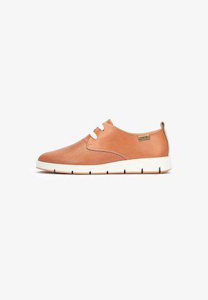 Zapatilla de cuero color marrón con diseño perforado, cordones blancos y suela blanca contrastante. Presenta una etiqueta de logo en el lateral.