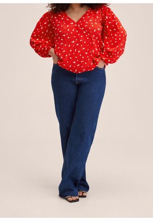 Blouse florale rouge avec un décolleté en V et des manches bouffantes, associée à un jean droit bleu marine, avec une texture subtile et une coupe décontractée.