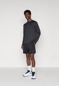 Fekete, hosszú ujjú sportpóló kis logóval, fekete hálós sorttal és fehér sneakerrel, fekete és kék kiegészítőkkel párosítva.