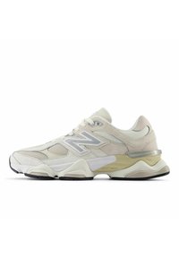 Baskets New Balance beige clair et crème avec panneaux en mesh et daim, semelle épaisse et logo argenté sur le côté.