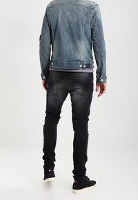 Světle modrá džínsová bunda se stříbrnými detaily, kombinovaná s černými slim džíny. Zadní pohled ukazuje švy a detaily kapes bundy.