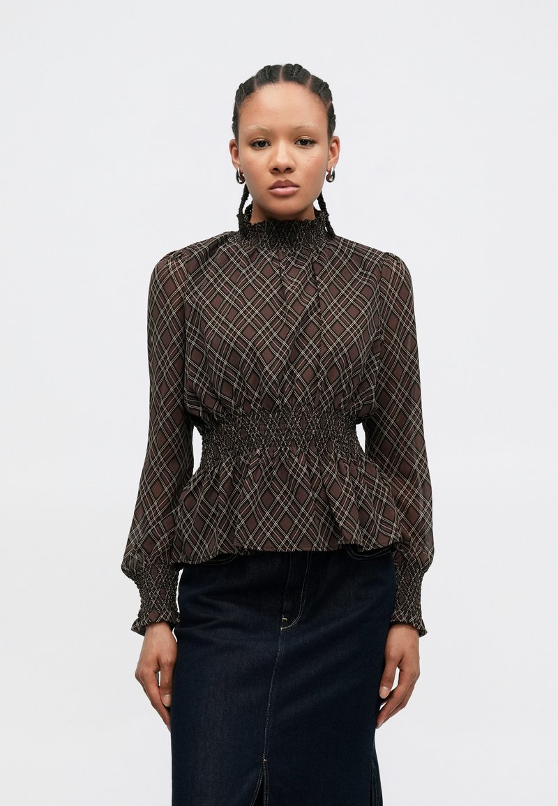 Brun mønstret bluse med høy hals, smokked midje og lange vide ermer, kombinert med et mørkt denimpanel.