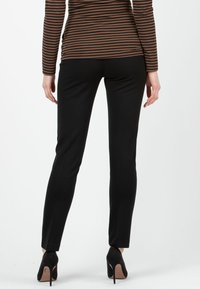 Schwarze, enganliegende Hose aus elastischem Stoff mit glatter Textur und schlanker Silhouette, kombiniert mit schwarzen High Heels.