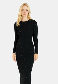 Schwarzes, geripptes Kleid mit langen Ärmeln und taillierter Silhouette, verziert mit kleinen, metallic-farbenen Akzenten, die gleichmäßig über den Stoff verteilt sind.