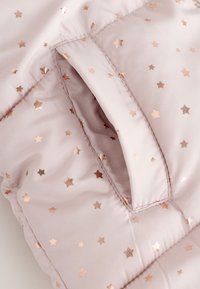 Svijetloružičasta pufer jakna sa sjajnim uzorkom ružičasto-zlatne zvijezde. Ima kontrastni džep i glatku, mekanu teksturu.