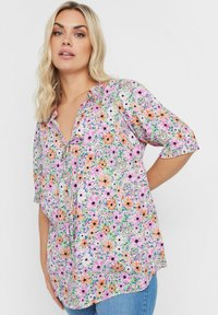 Blommig blus med korta ärmar, med ett flerfärgat blommönster på en ljus bakgrund. Inkluderar en knytning vid halsen och mjuk tyg.