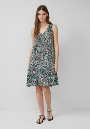 Mouwloze jurk in zwart met een geometrisch patroon in turquoise, wit en bruin. Flared rok en zachte stof. Schoeisel: zwarte sandalen.