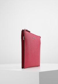 Red synthetic leather clutch bag with a smooth texture, rectangular shape, and a metal zipper. Features subtle logo detailing on the front.