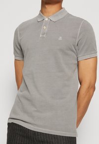 Grå bomullspolo med klassisk krage, treknappars placket och broderad logotyp på bröstet. Korta ärmar och en avslappnad passform.
