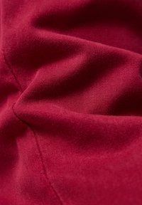 Red fabric with visible stitching and soft folds, showing texture and weave details.