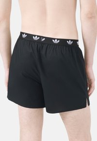 Svarta simshorts med en texturerad midja som har upprepade vita loggopunkter. Löst snitt, sidofickor vid fållen för ökad komfort.