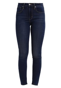 Jeans ajustados de mezclilla azul oscuro, de cintura alta, con diseño de cinco bolsillos y un ligero desvanecimiento a lo largo de las piernas.