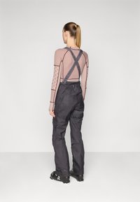 Black ski overalls with adjustable straps, two side pockets, and a loose fit. Lightweight, durable material with a textured finish.