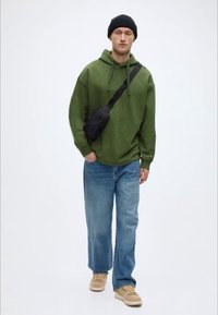 Πράσινο φούτερ με κουκούλα, άνετο μπλε τζιν παντελόνι, μπεζ αθλητικά παπούτσια και μαύρη τσάντα χιαστί. Διαθέτει χαλαρή εφαρμογή και μαλακή υφή.